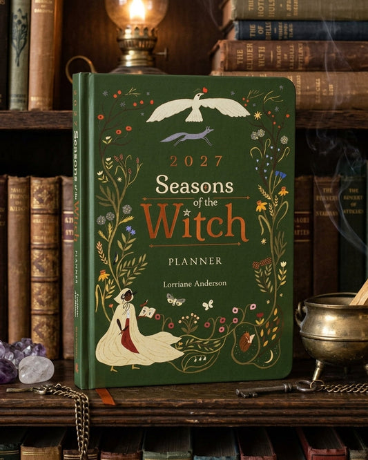 A hardcover planner titled "2027 Seasons of the Witch Planner" by Lorrene Anderson, standing on a wooden shelf surrounded by old books, a brass candelabra, crystals, and a small bronze cauldron.