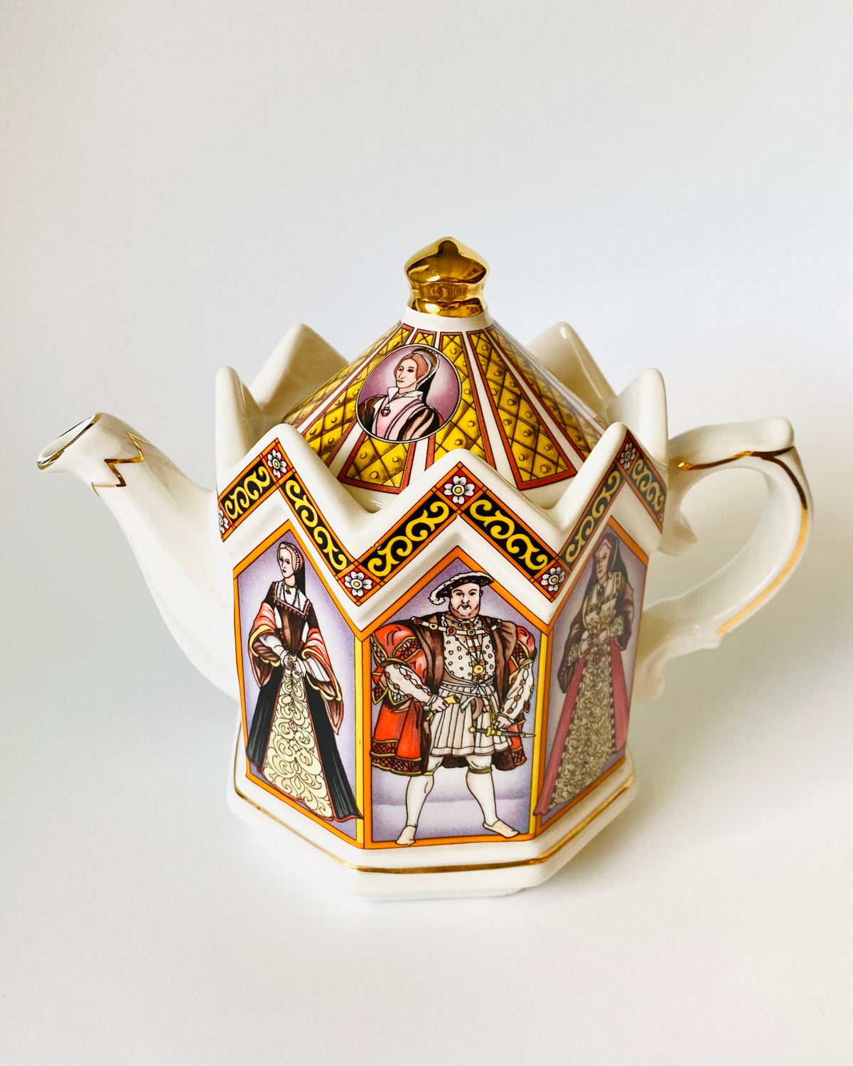 A decorative white porcelain teapot with a pointed octagonal shape, featuring gold trim and colorful illustrated panels of historical figures on its sides, set against a plain white background.