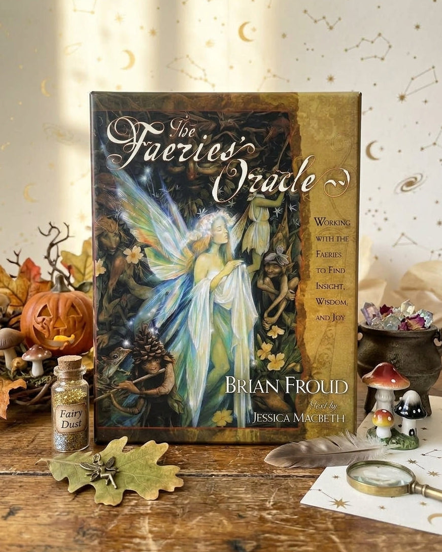 The 'Los Faeries Oracle' deck box by Brian Froud is displayed on a rustic wooden table surrounded by autumn-themed props including a small bottle of fairy dust, a carved pumpkin, leaves, and miniature mushrooms against a cream background with gold moon and star illustrations.