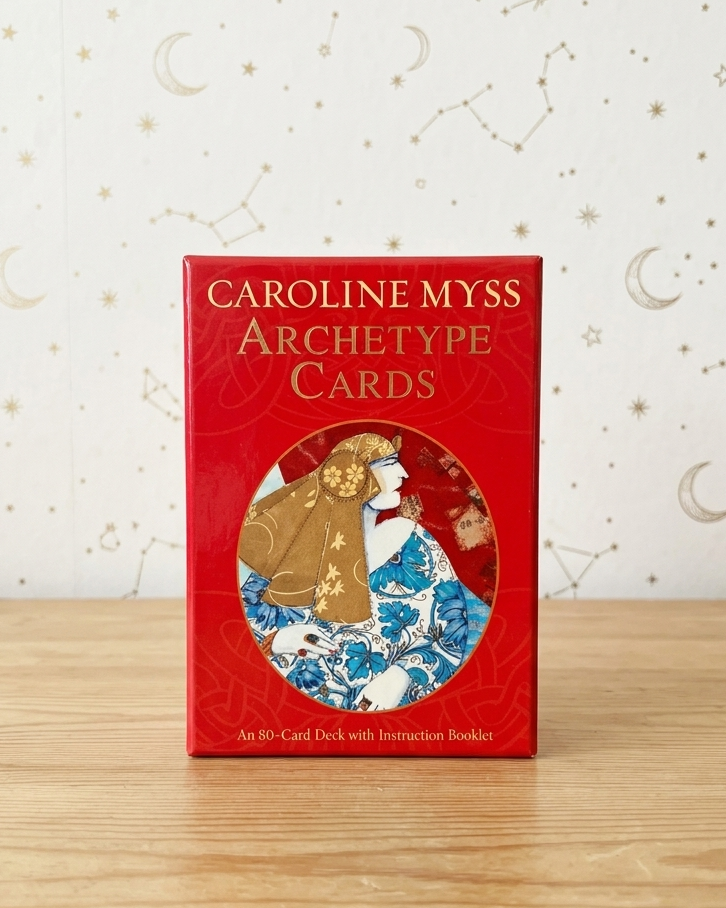Caroline Myss Archetype Cards deck box standing upright on a light wood surface against a white wall with gold celestial patterns.