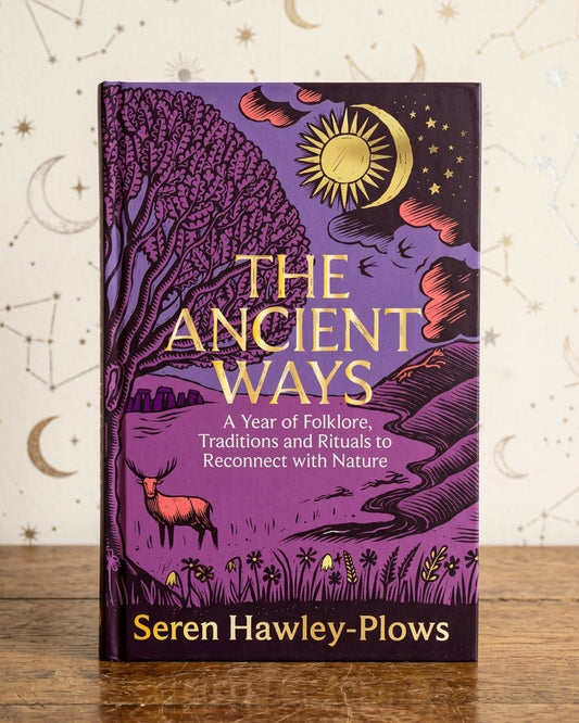 The Ancient Ways: A Year of Folklore, Traditions and Rituals to Reconnect with Nature book by Seren Hawley-Plows, standing upright on a wooden surface against a cream-colored background decorated with celestial patterns.