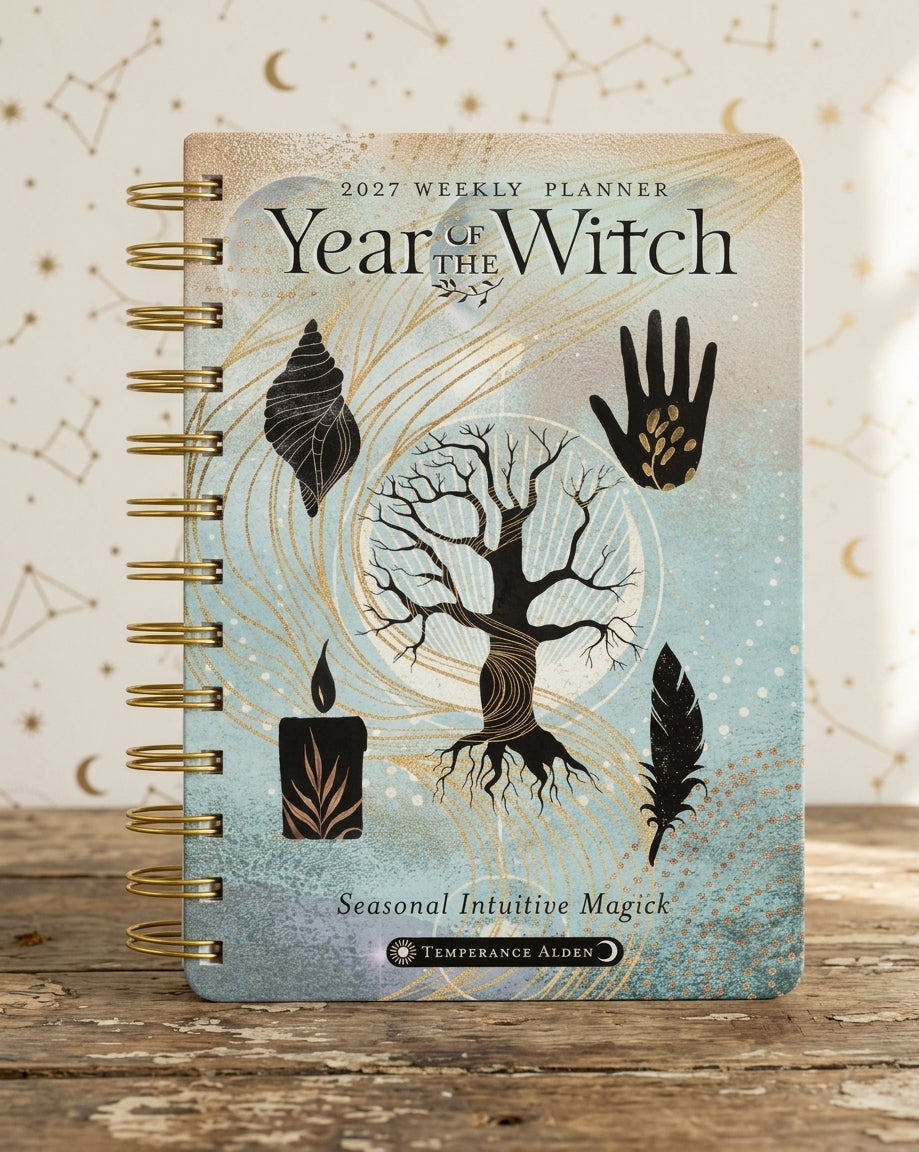 A spiral-bound 2027 Weekly Planner titled 'Year of the Witch' by Temperance Alden, featuring a mystical design with a tree, candles, feathers, and a shell on a light blue and beige background, displayed on a rustic wooden surface.