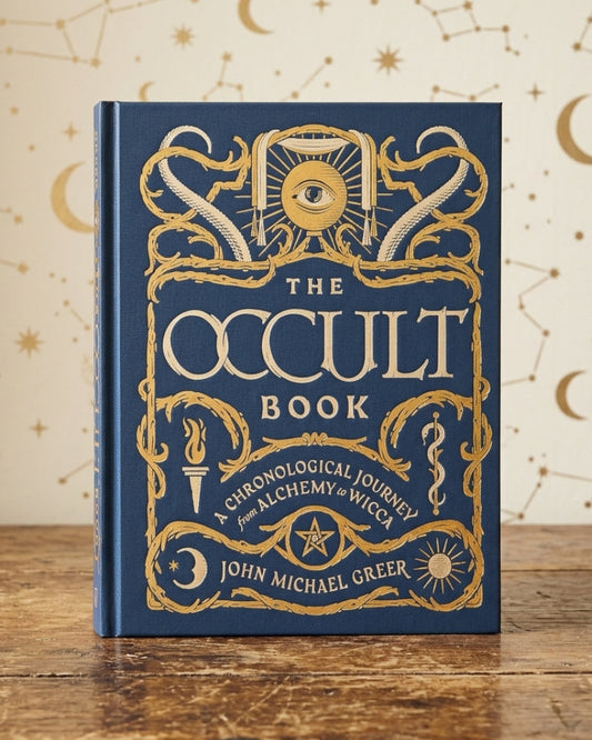 The Occult Book by John Michael Greer, a hardcover book with a deep blue cover and ornate gold foil illustrations, standing on a rustic wooden table against a cream-colored background decorated with gold celestial patterns.