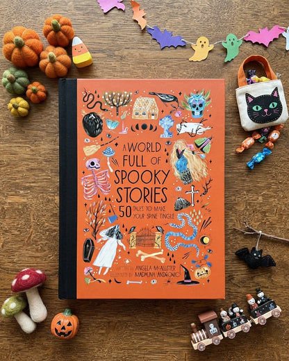 A book titled 'A World Full of Spooky Stories' lies on a wooden surface surrounded by Halloween-themed props including miniature pumpkins, candy corn, ghosts, mushrooms, a black cat pouch, and a toy train.