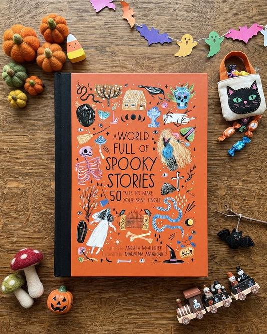 A book titled 'A World Full of Spooky Stories' lies on a wooden surface surrounded by Halloween-themed props including miniature pumpkins, candy corn, ghosts, mushrooms, a black cat pouch, and a toy train.