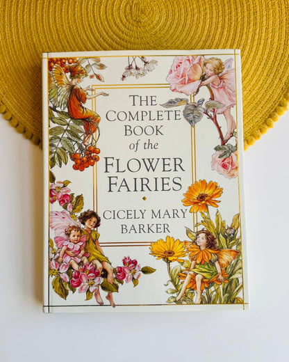 The Complete Book of the Flower Fairies by Cicely Mary Barker, featuring a vintage-style illustrated cover with fairies and flowers, displayed on a white surface with a yellow woven placemat in the background.