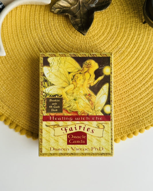 Healing with the Fairies Oracle Cards deck box by Dorcen Vuitne, PhD, displayed on a yellow woven placemat with decorative props.