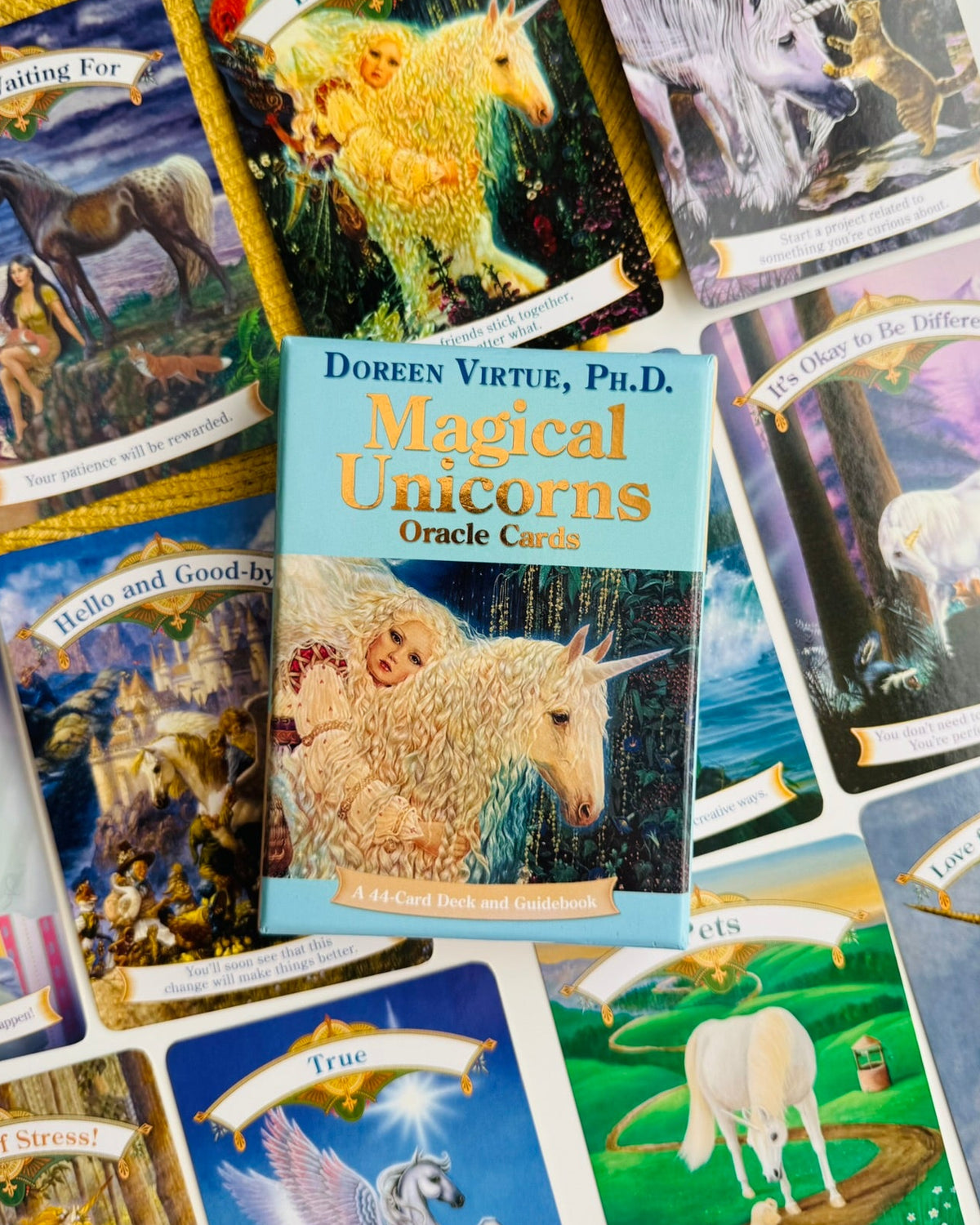 A spread of oracle cards from Doreen Virtue's 'Magical Unicorns Oracle Cards' deck, featuring colorful unicorn and fantasy illustrations on a light surface with a yellow textured blanket underneath some cards.