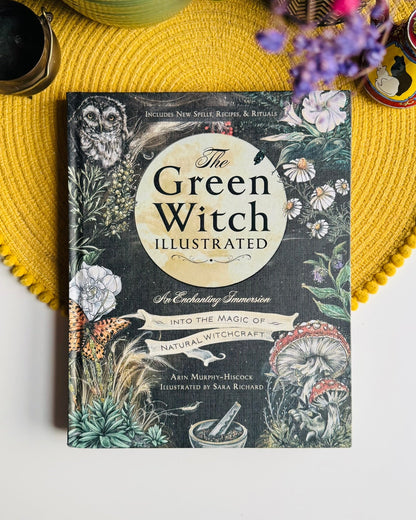 The Green Witch Illustrated book by Asin Murphy-Hieuce and Sarah Richard, featuring an illustrated cover with a dark background and botanical designs, styled on a yellow woven placemat with decorative props.