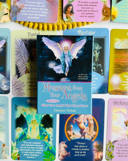 A boxed card deck titled "Messages from Your Angels" by Daren Virtue is centered in front of several colorful angel and scripture cards arranged on a white surface.