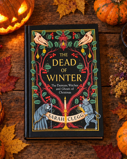 A book titled "The Dead of Winter" by Sarah Clelog lies on a round yellow woven placemat. The cover features a black background with ornate red and gold decorative illustrations and text.