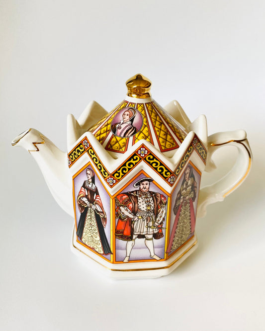 A decorative white porcelain teapot with a pointed octagonal shape, featuring gold trim and colorful illustrated panels of historical figures on its sides, set against a plain white background.
